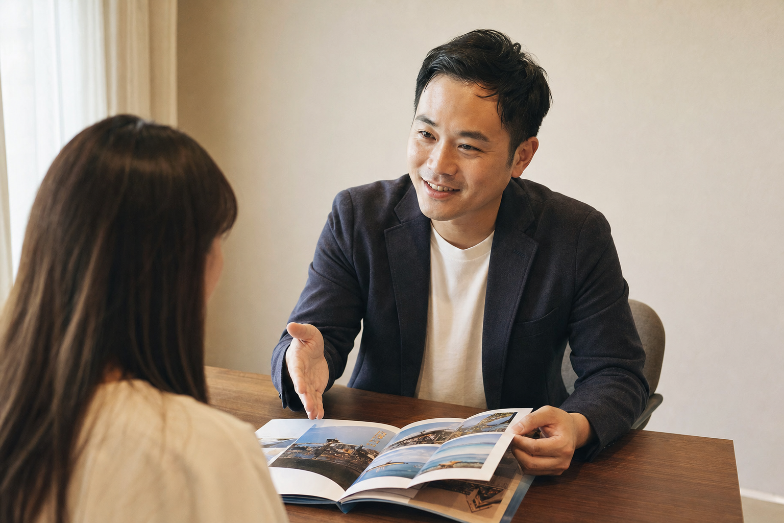 旅行社業務坐在客人對面，翻開一本印刷成冊的行程手冊，笑著向客人介紹行程